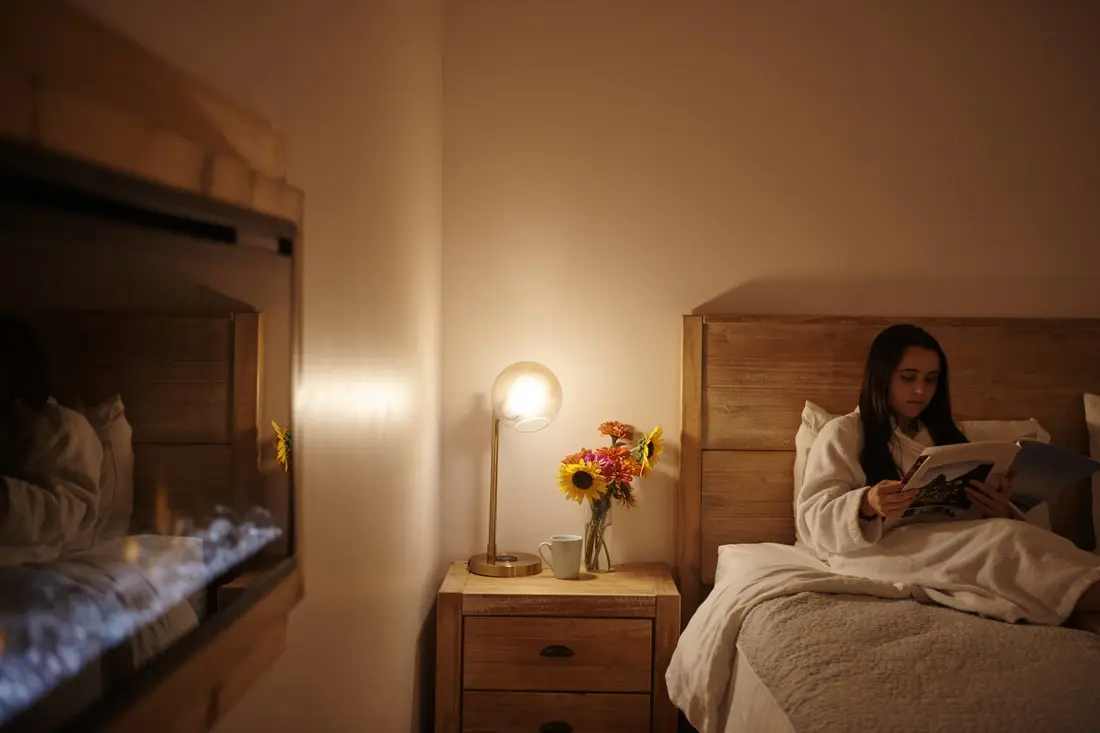 A guest reading in bed by lamplight, the fireplace glowing